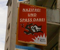 Plakat 'Nazifrei und Spaß dabei' von Jusos Berlin, Motiv: Hakenkreuz zerschlagende Hand; Hintergrund rot; vor Häuserwand